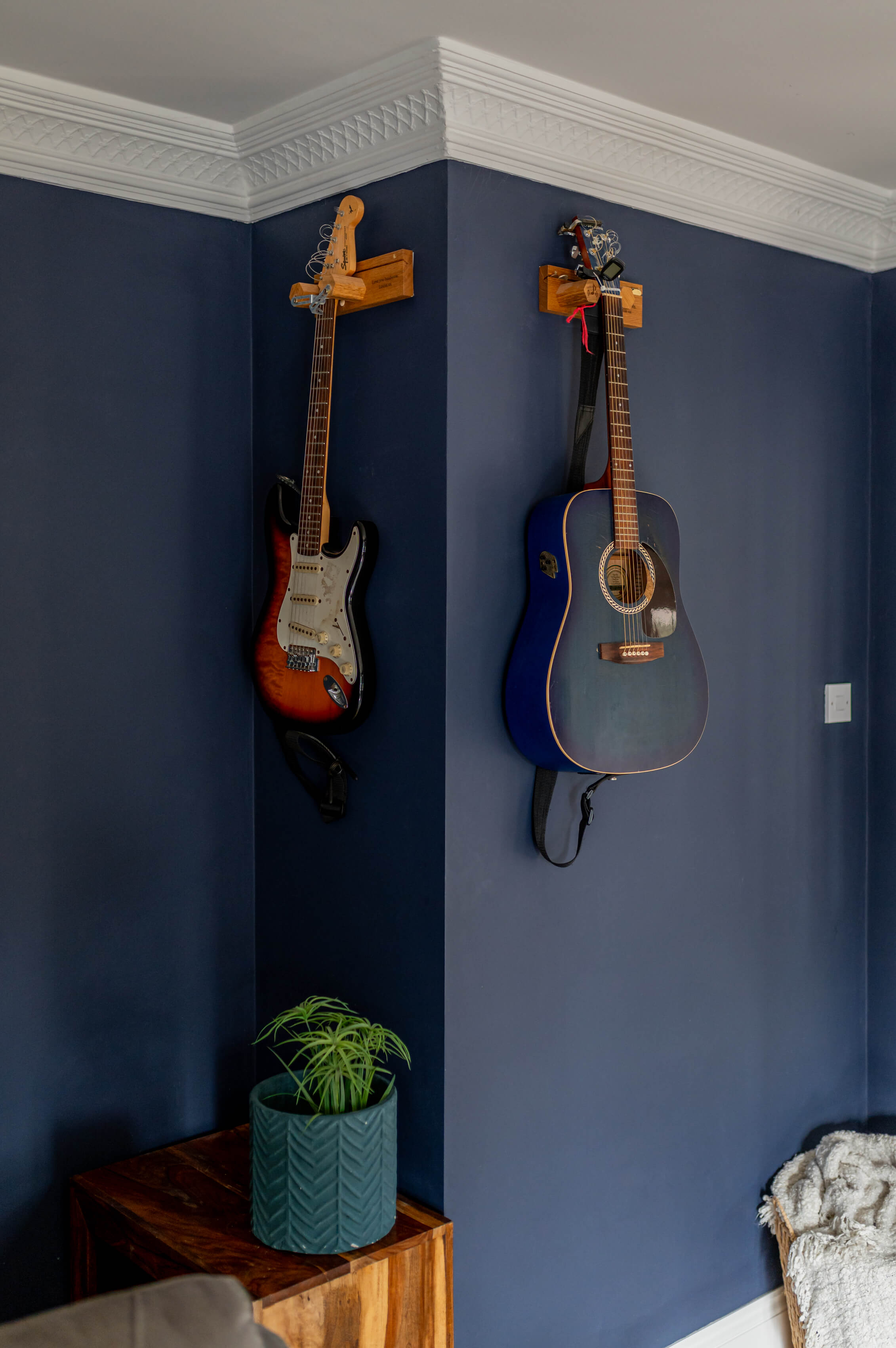 a living room with dark navy walls. Two guitars are hung on the walls. Ornate, traditional coving on the ceiling.